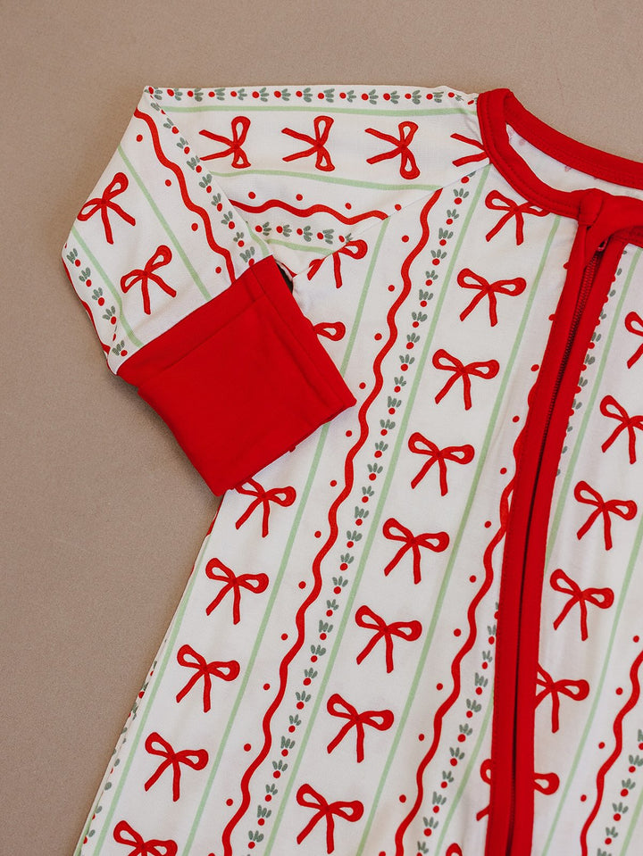 Detail of the Christmas Bows romper laid flat, showing the red neckline, sleeve cuff, zipper and bow print.