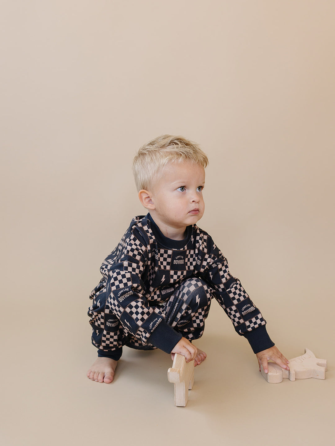 Toddler crouching beside wooden toys in the Long Live Boyhood cotton top and joggers.
