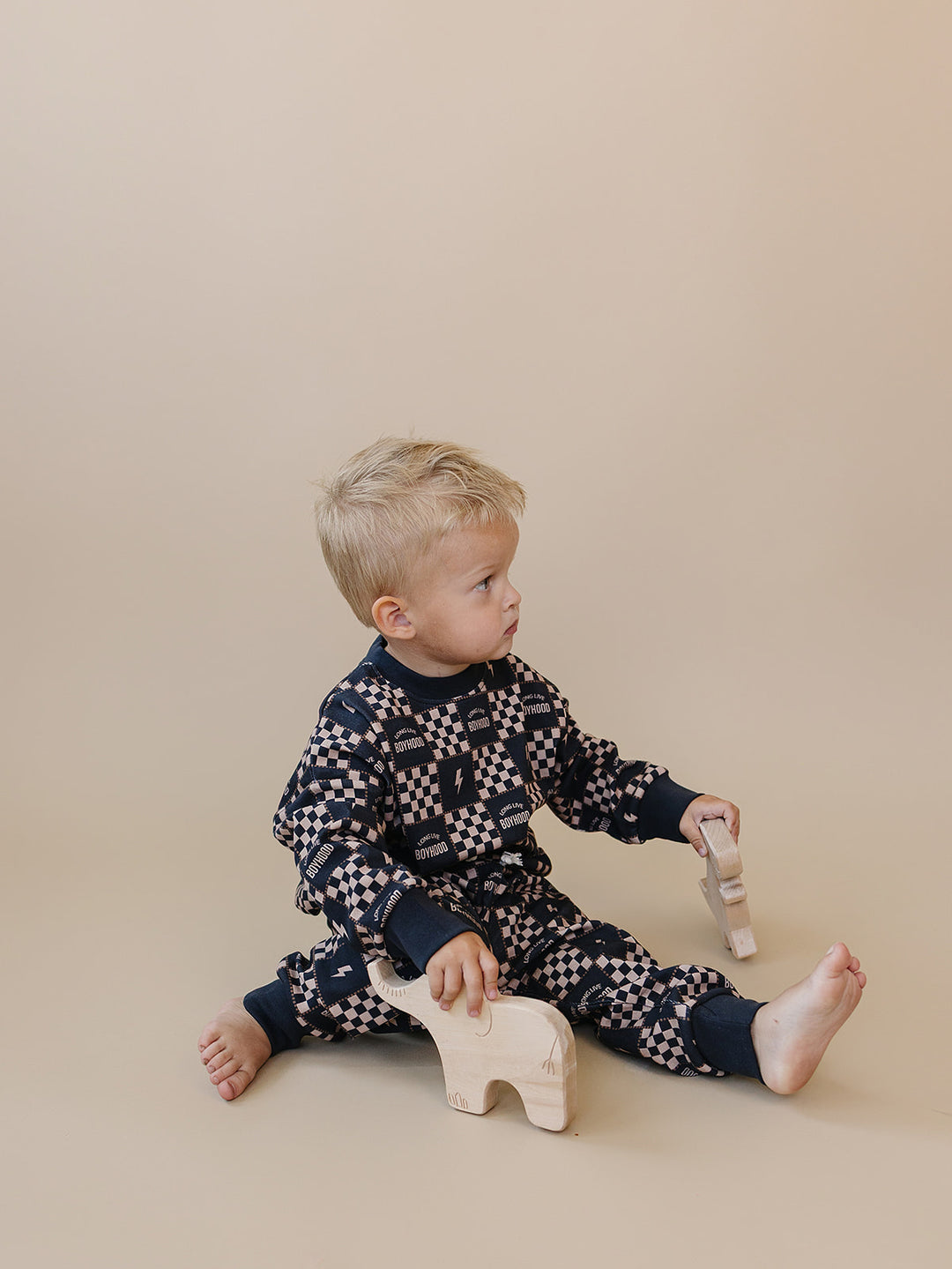 Toddler sitting with wooden toys while wearing the Long Live Boyhood checkered cotton jogger set.
