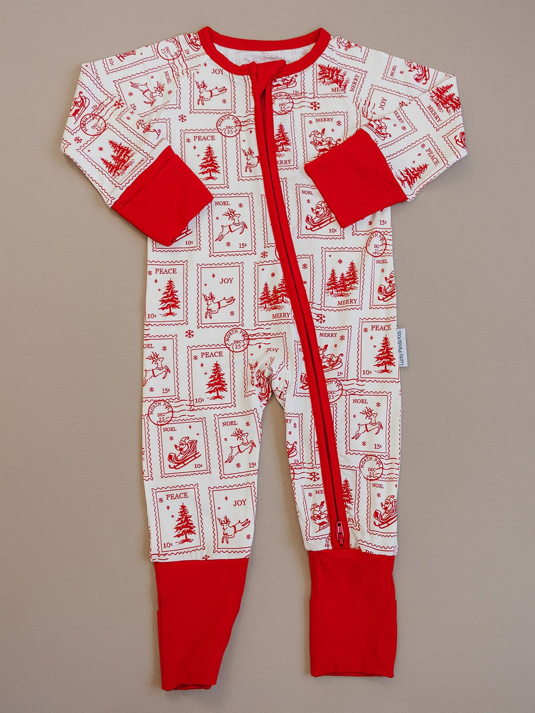North Pole Stamps Christmas zip romper laid flat, showing long sleeves, red cuffs and a cream holiday stamp print.
