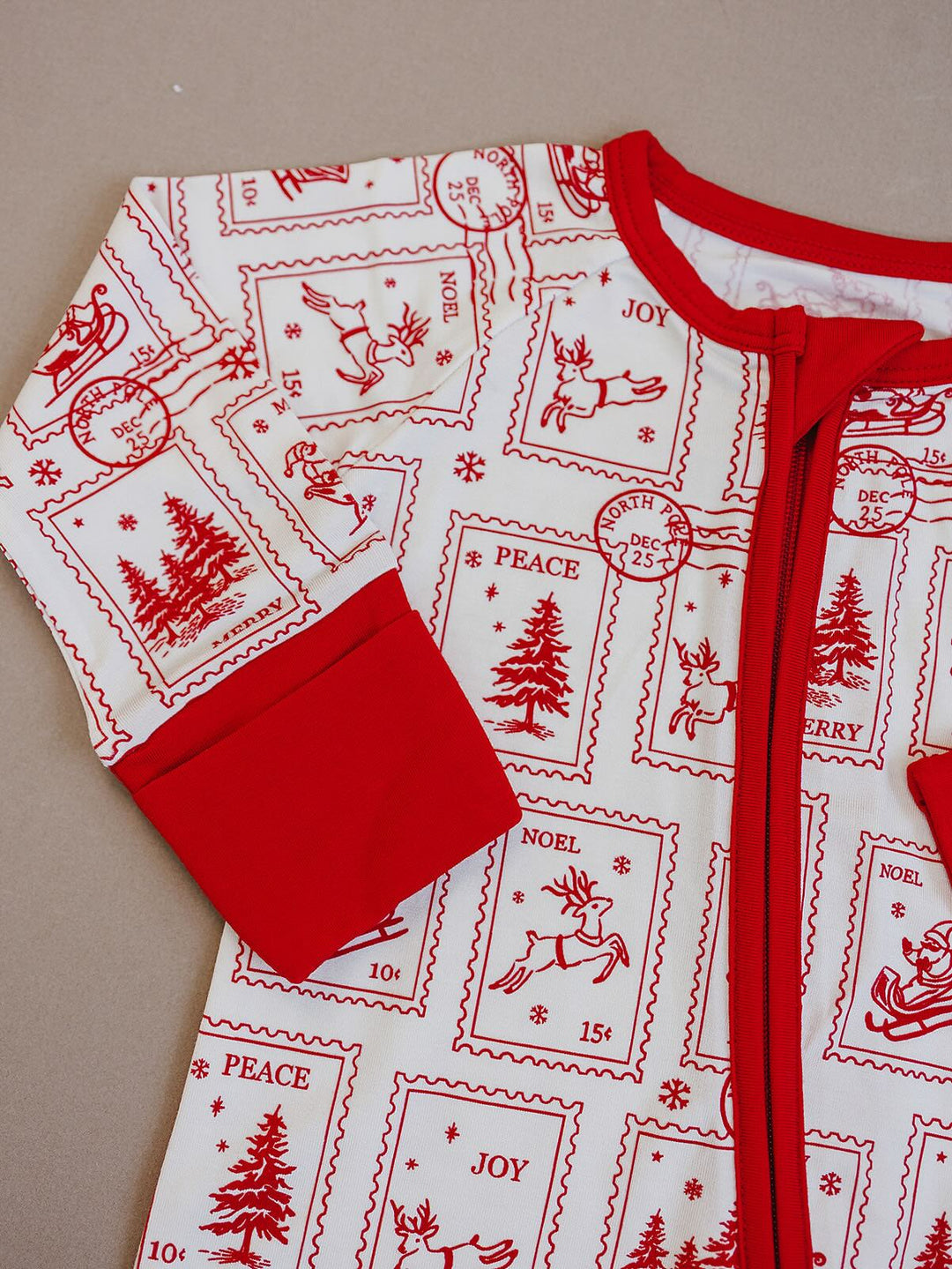 Detail of the North Pole Stamps romper showing the red neckline, zipper, sleeve cuff and holiday print.