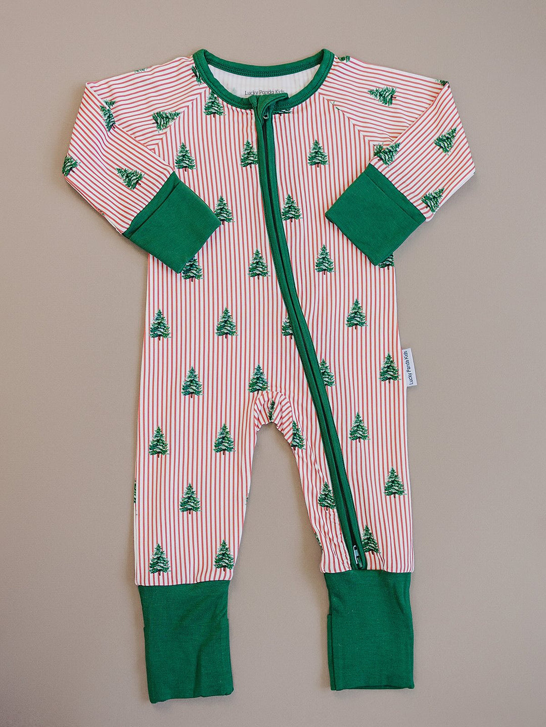 Magical Trees zip romper laid flat, showing Christmas trees over red and white stripes with green trim.