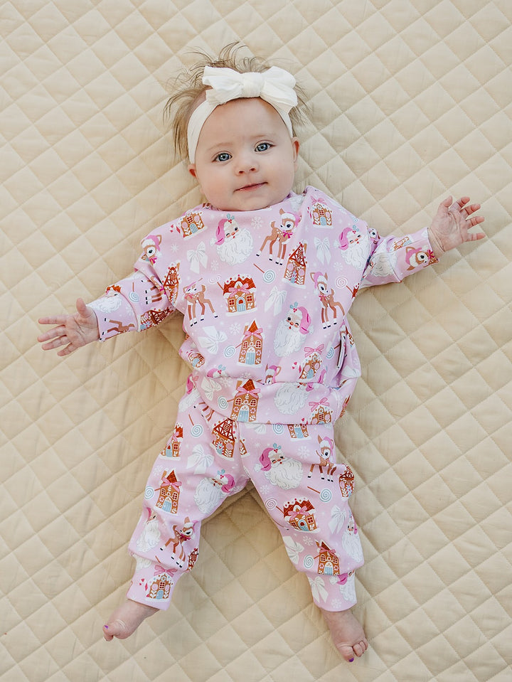 Baby wearing a white bow headband and Pink Christmas jogger set with legs stretched out on a quilt.
