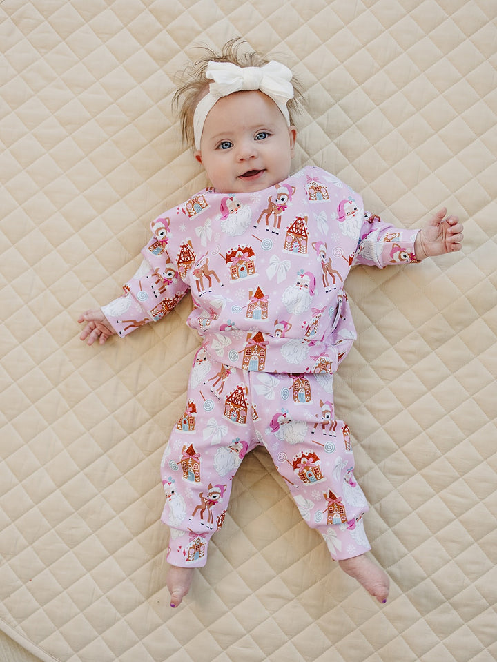 Full length view of a baby on a quilt in the Pink Christmas jogger set with a white bow headband.
