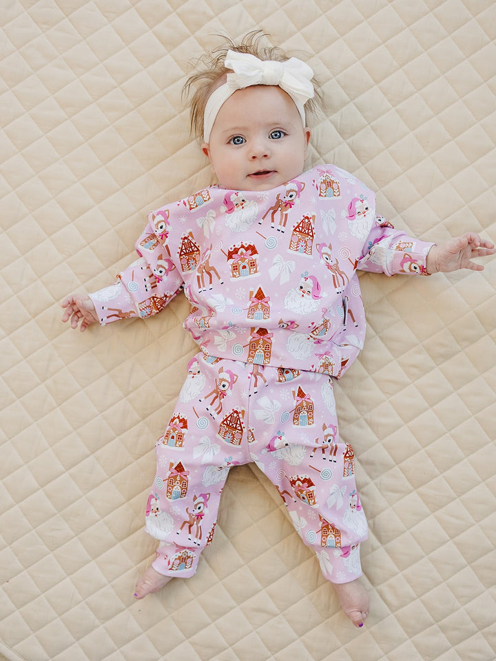 Baby lying with arms out on a cream quilt in the Pink Christmas top and matching pants.