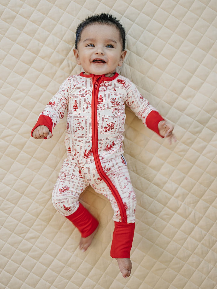 Smiling baby lying on a quilt in the North Pole Stamps Christmas romper with feet uncovered.