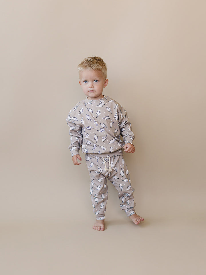 Toddler boy standing against a beige background in the Latte Bolts jogger set, showing the relaxed fit.