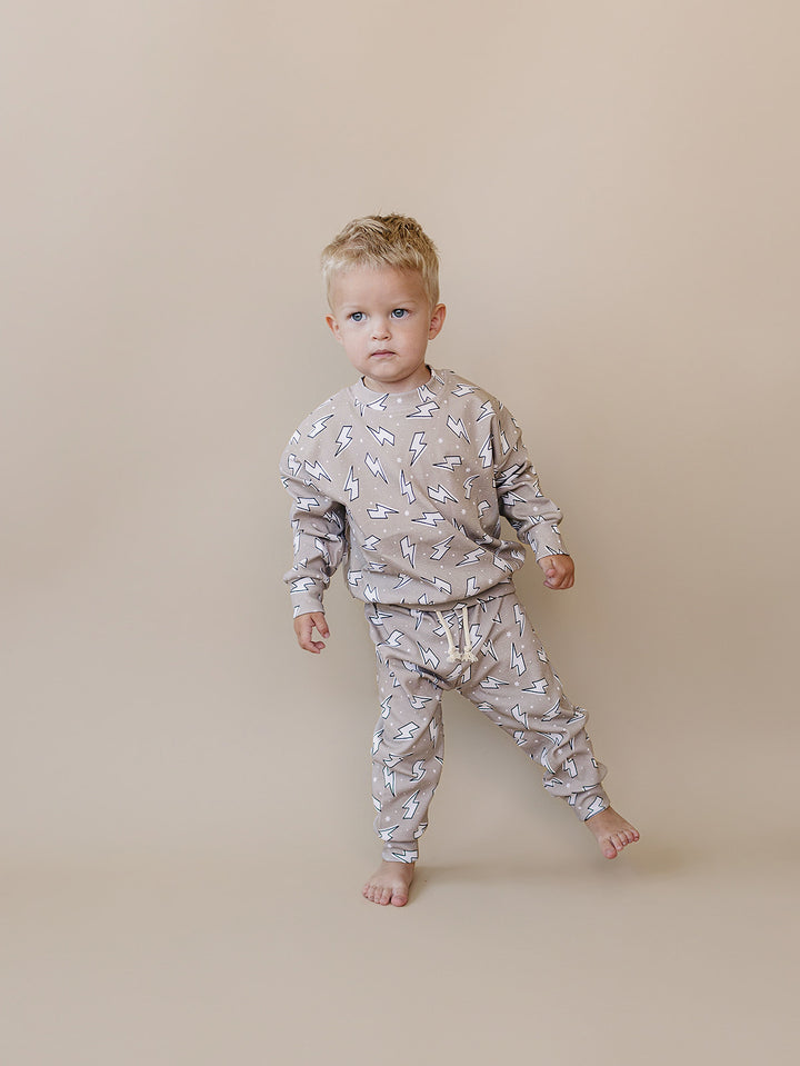 Toddler boy stepping playfully while wearing the Latte Bolts jogger set, showing its comfortable fit for movement.
