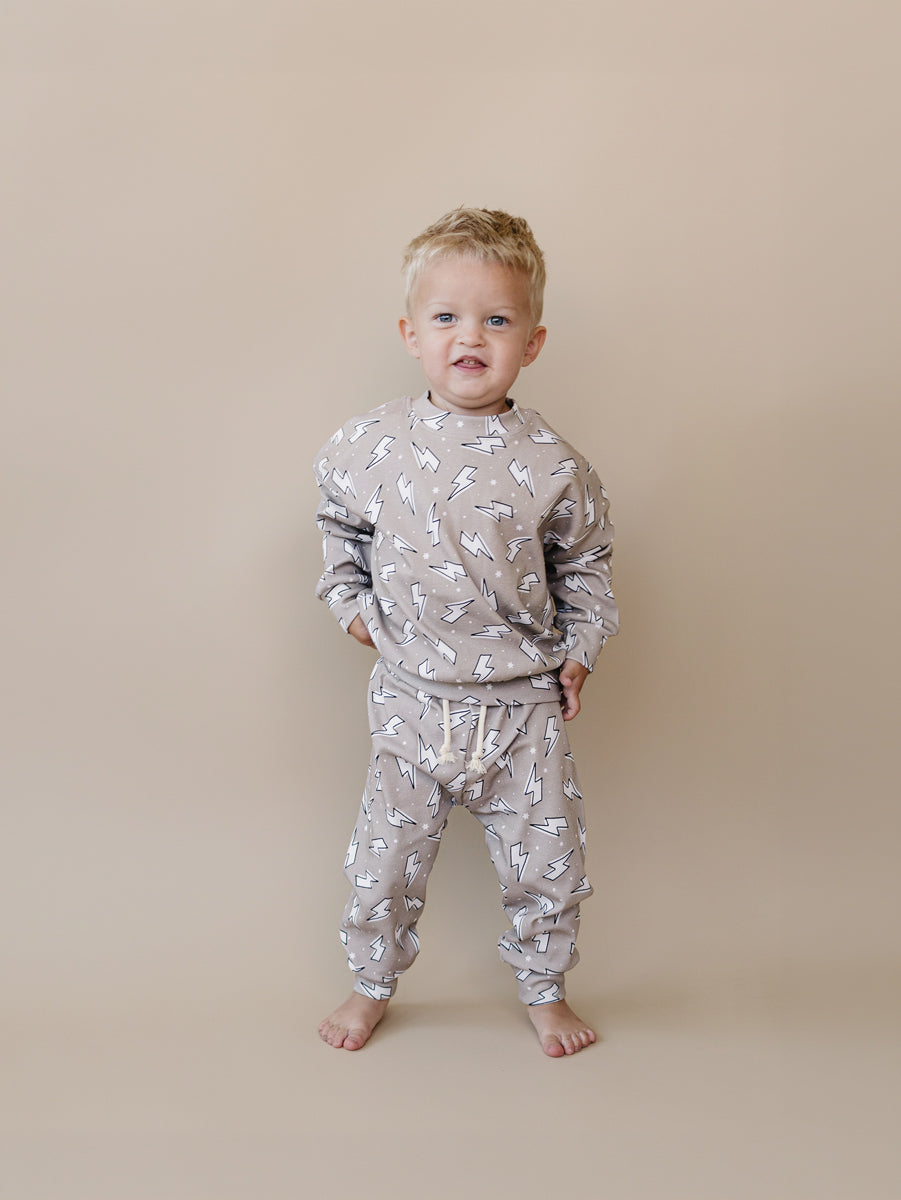 Toddler boy modeling the Lucky Panda Kids Latte Bolts cotton jogger set in a warm taupe lightning bolt print.