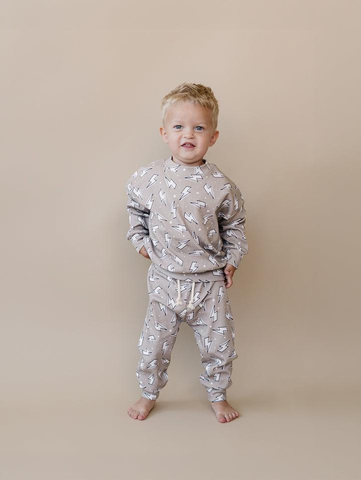 Toddler boy modeling the Lucky Panda Kids Latte Bolts cotton jogger set in a warm taupe lightning bolt print.