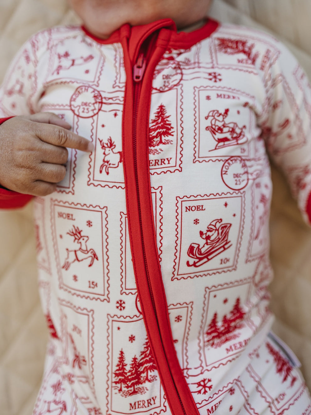 Close up of the North Pole Stamps romper showing the red front zipper and Christmas postage stamp print.