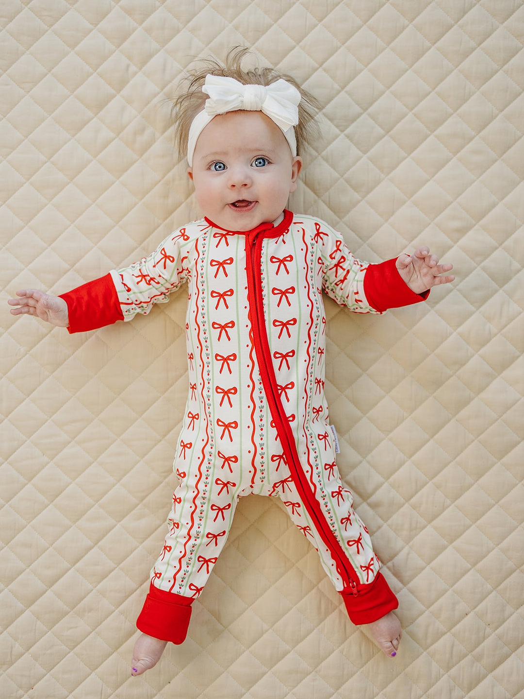 Baby lying with arms out in the Christmas Bows romper with red trim and feet uncovered.