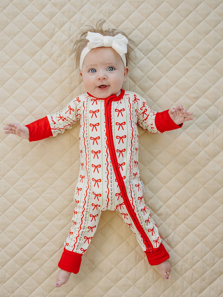 Baby lying with arms out in the Christmas Bows romper with red trim and feet uncovered.