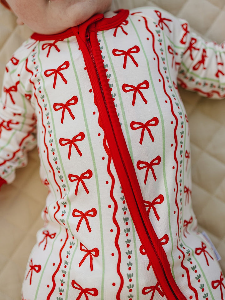Close up of the Christmas Bows romper showing the red zipper and rows of red bows on a cream background.