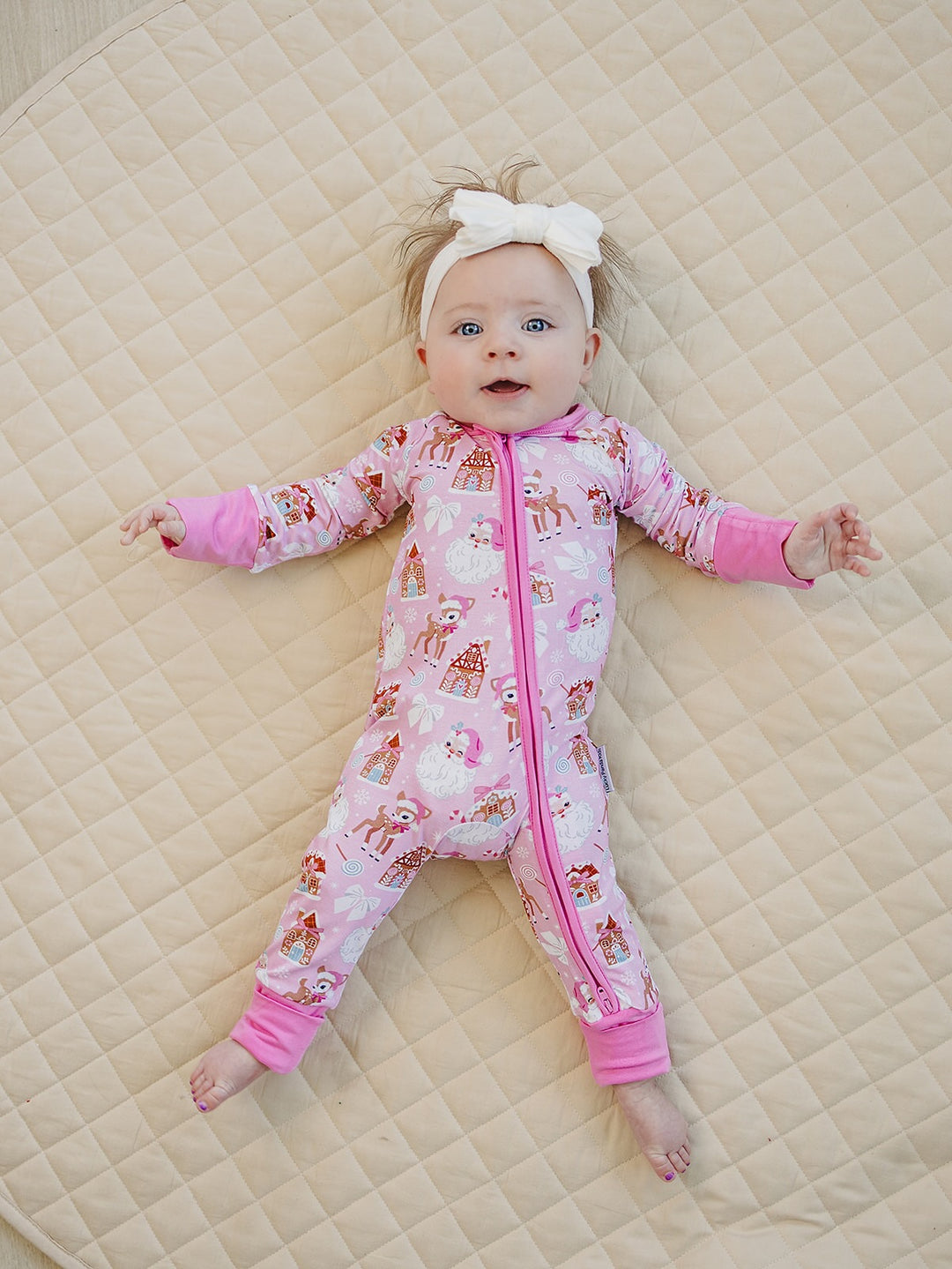 Baby lying with arms out in the Pink Christmas romper, showing the holiday print and pink cuffs.