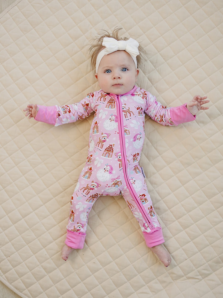 Front view of a baby on a cream quilt wearing the Pink Christmas romper with feet uncovered.