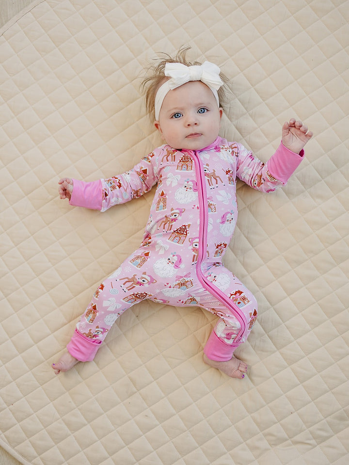 Baby bending one knee while lying on a quilt in the Pink Christmas romper and a white bow headband.