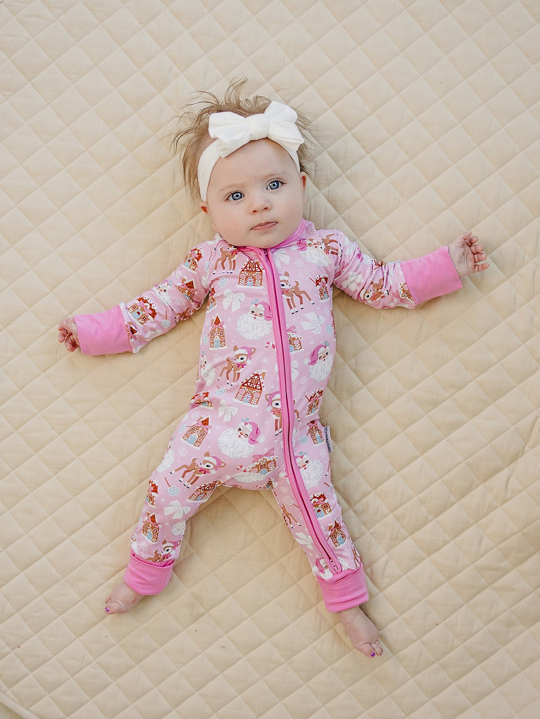 Baby looking to the side on a cream quilt while wearing the Pink Christmas zip romper with pink trim.