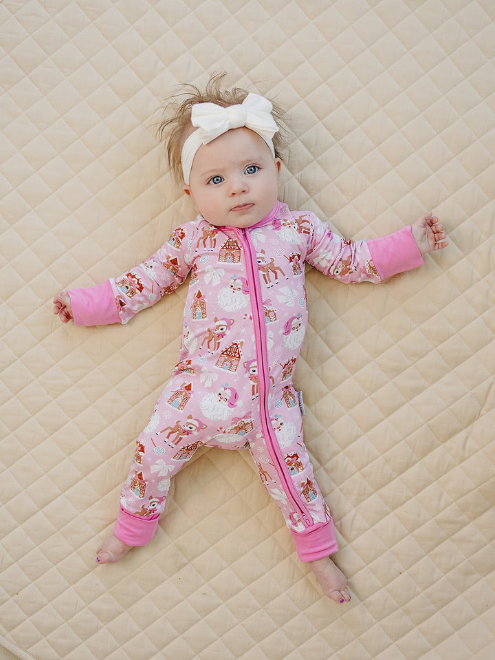 Baby looking to the side on a cream quilt while wearing the Pink Christmas zip romper with pink trim.