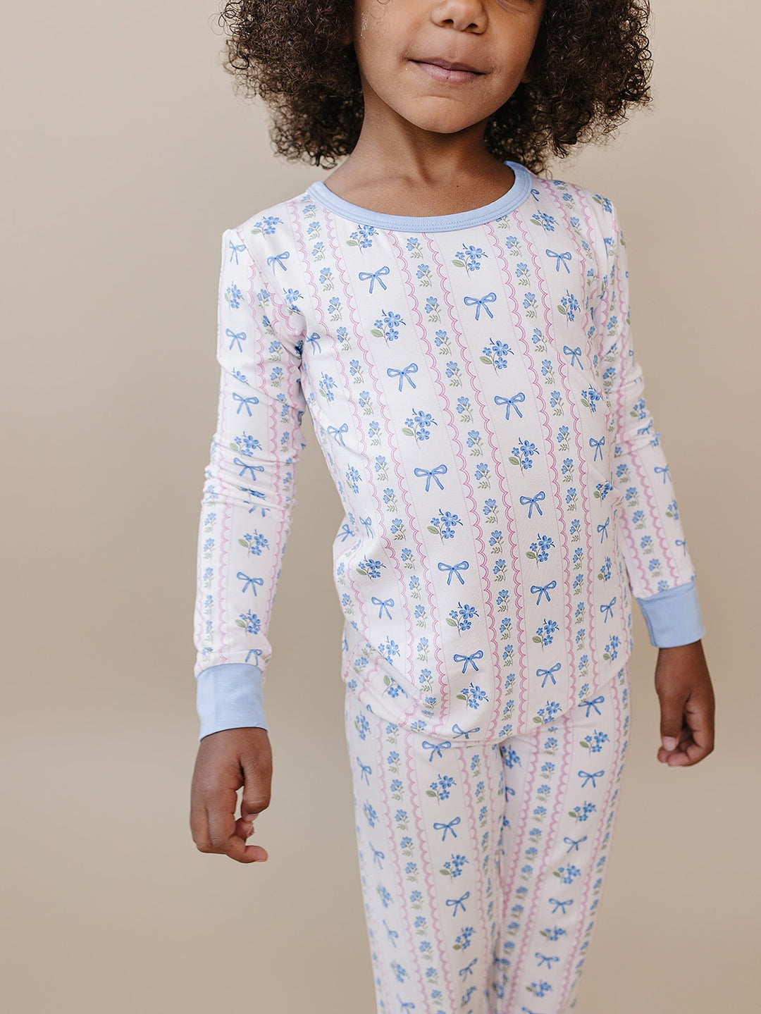 Baby facing the camera on a cream quilt in the Whimsy Bloom floral cotton top and matching pants.