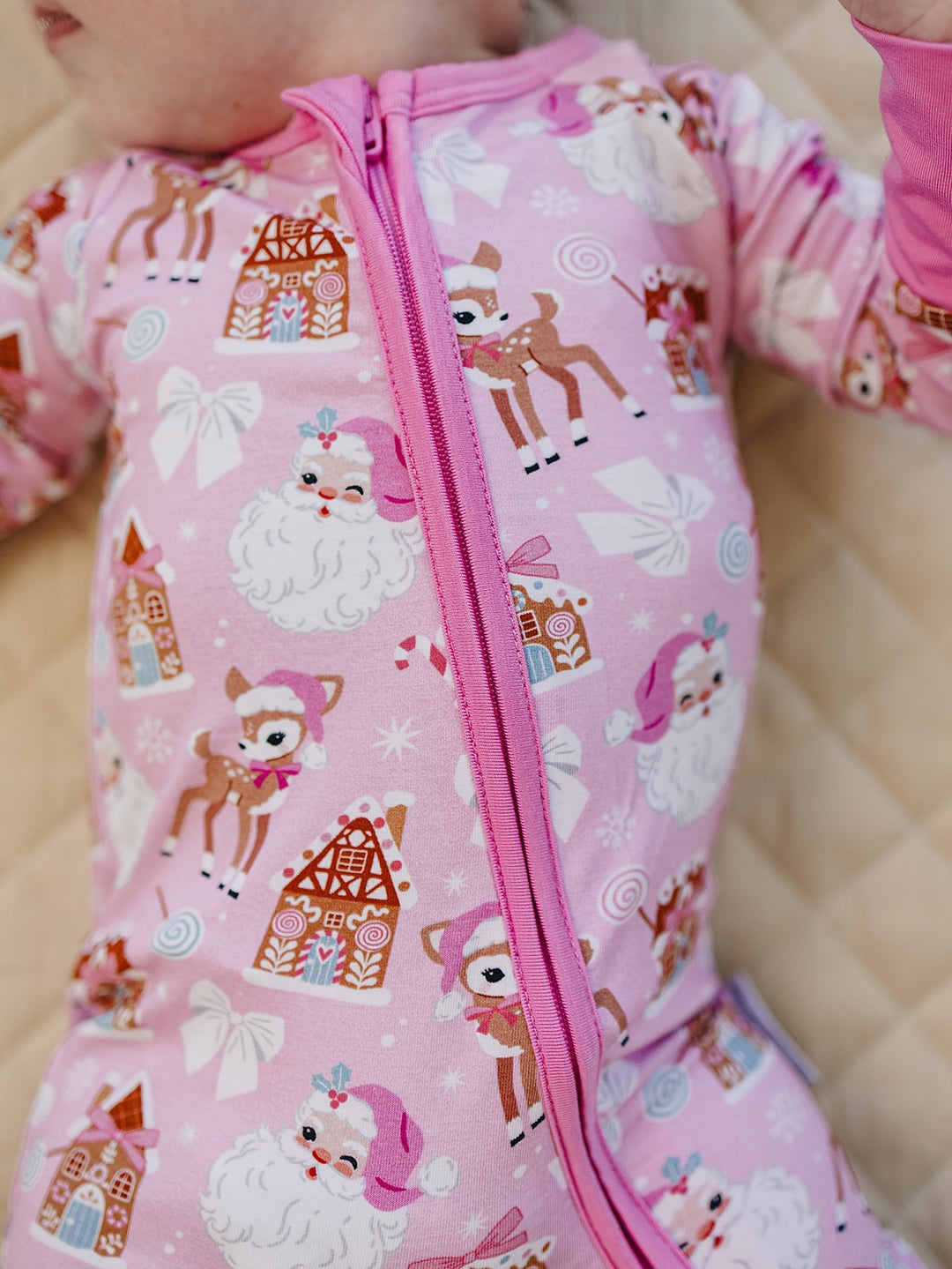 Close up of the Pink Christmas romper showing the pink zipper, Santa faces, reindeer and gingerbread houses.