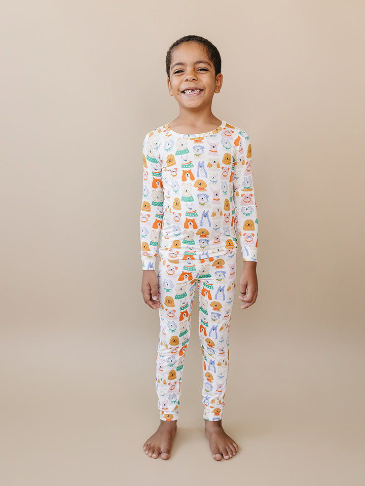 Smiling child standing with arms at their sides in the Puppy Club dog-print bamboo two-piece set.