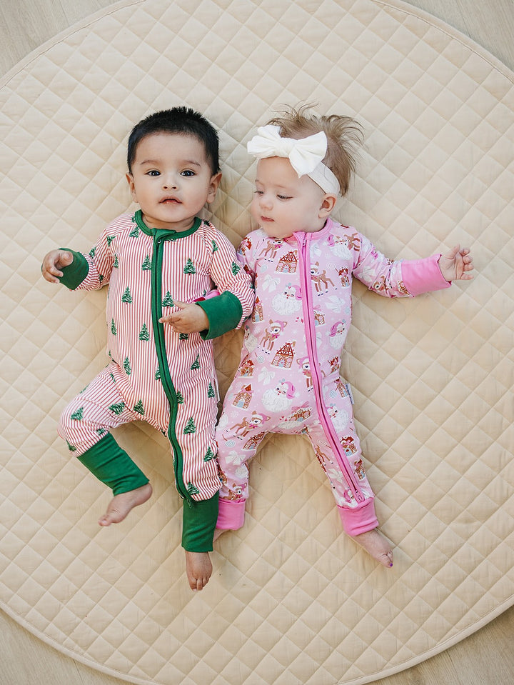 Two babies lying together on a quilt, one wearing the Magical Trees romper and the other a pink holiday outfit.