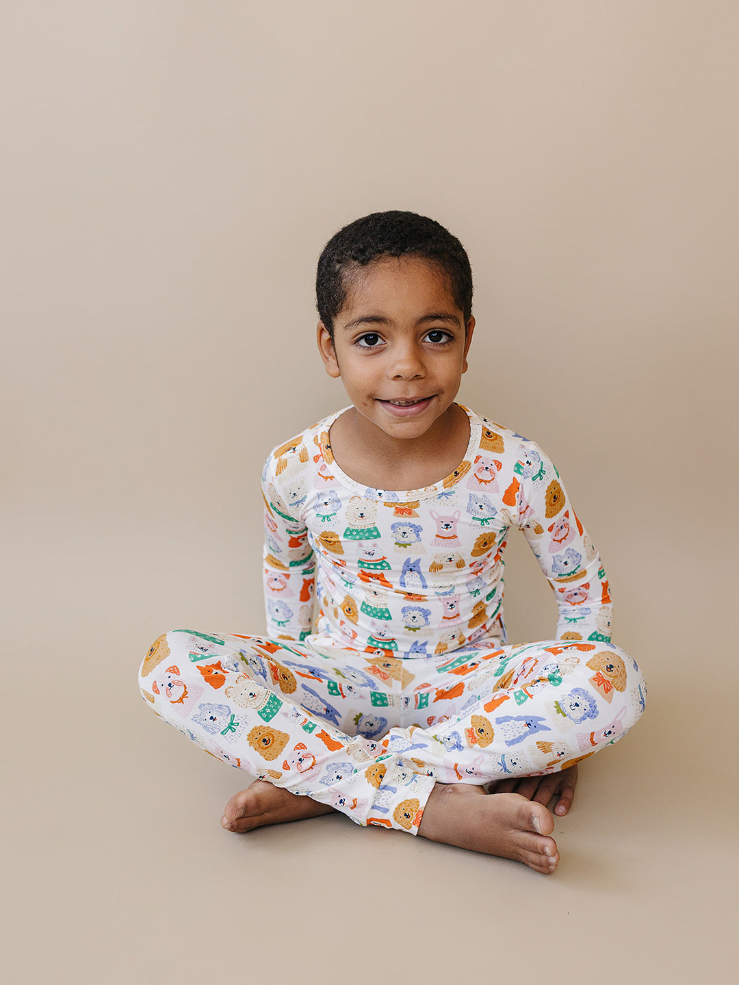 Front view of a child seated cross-legged in the Puppy Club bamboo pajama set.