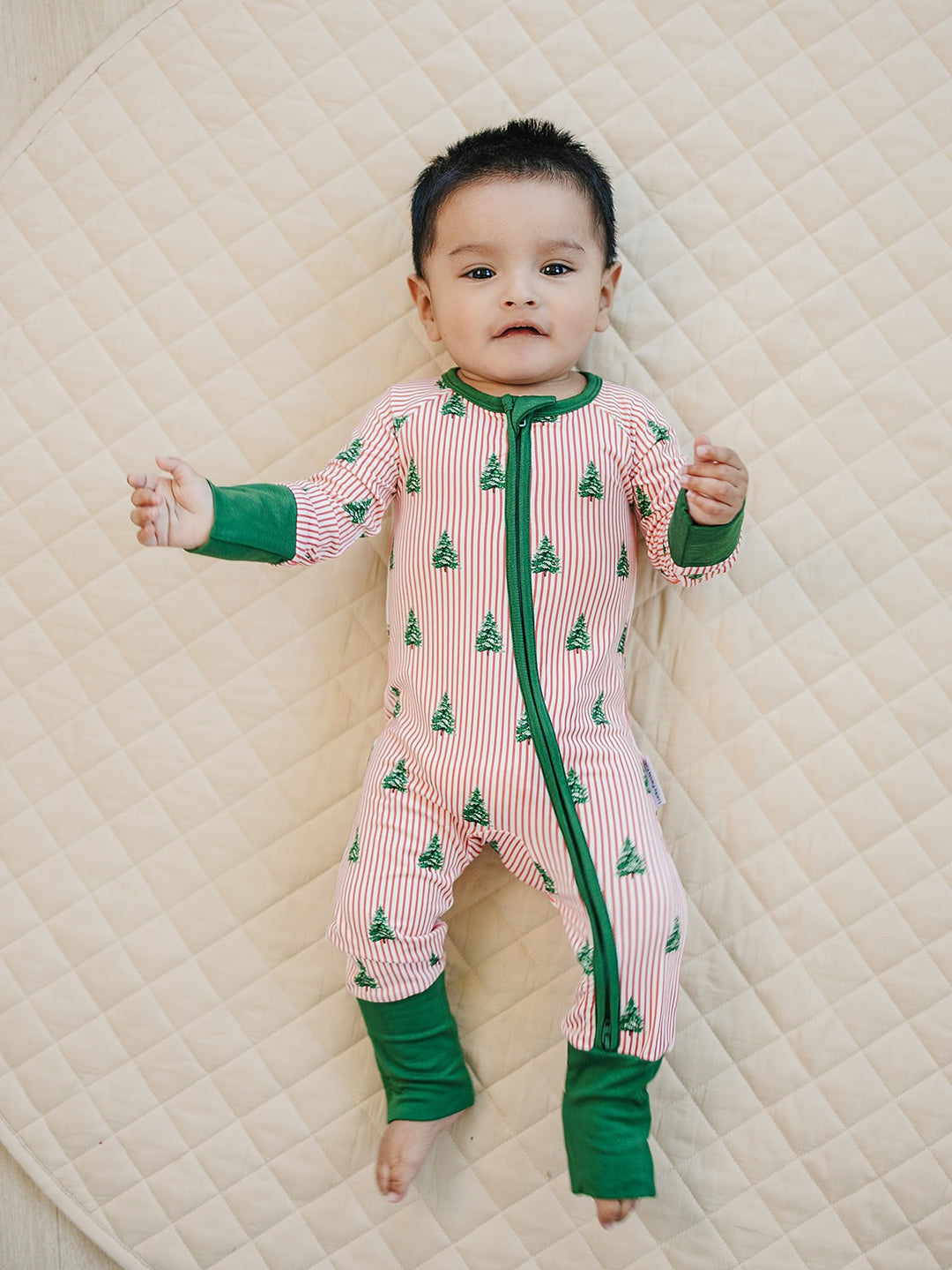 Baby lying with arms out in the Magical Trees striped Christmas romper on a cream quilt.