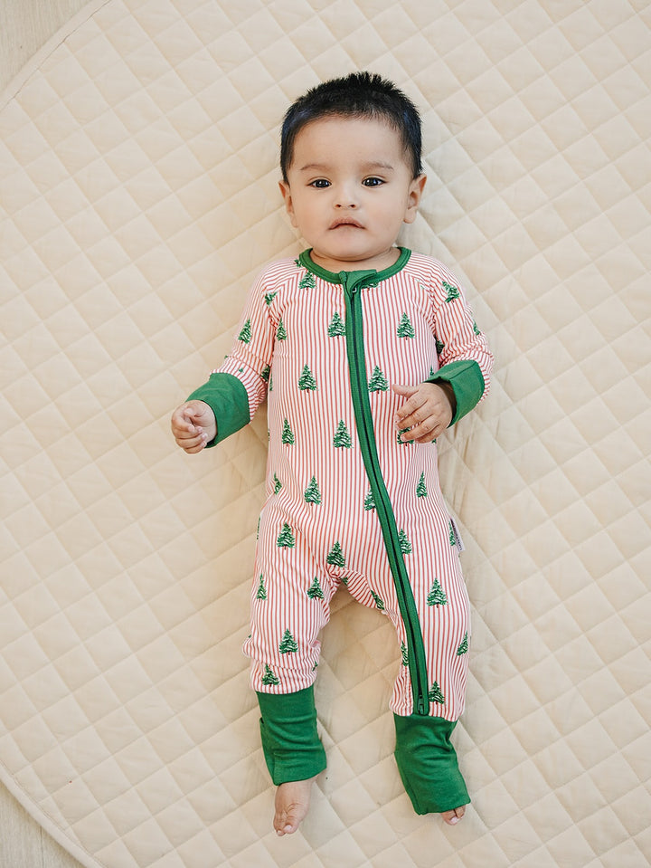 Full length view of a baby on a quilt wearing the Magical Trees zip romper with green wrist and ankle cuffs.