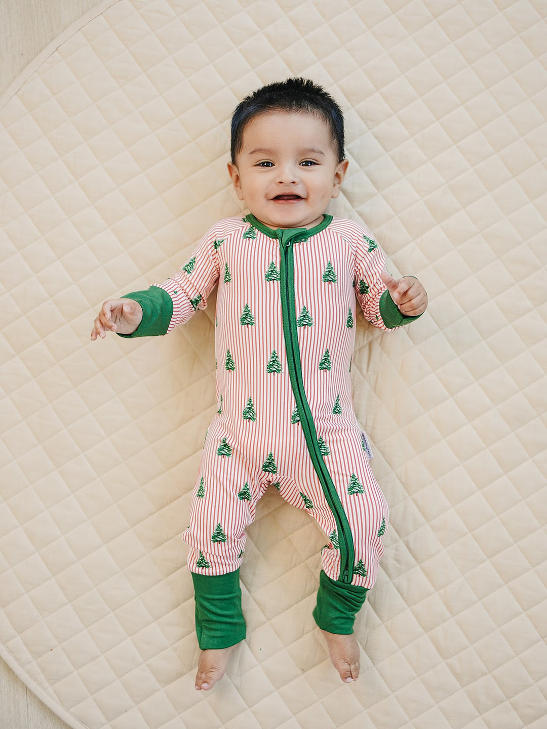 Baby on a cream quilt wearing the Magical Trees zip romper with green Christmas trees and green trim.