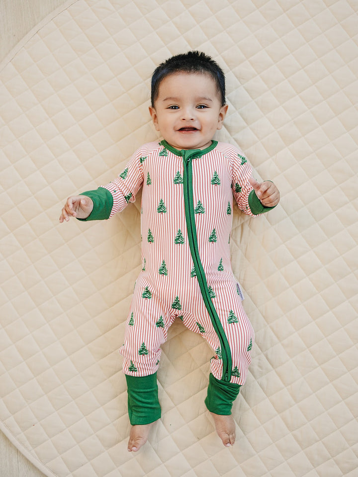 Baby on a cream quilt wearing the Magical Trees zip romper with green Christmas trees and green trim.