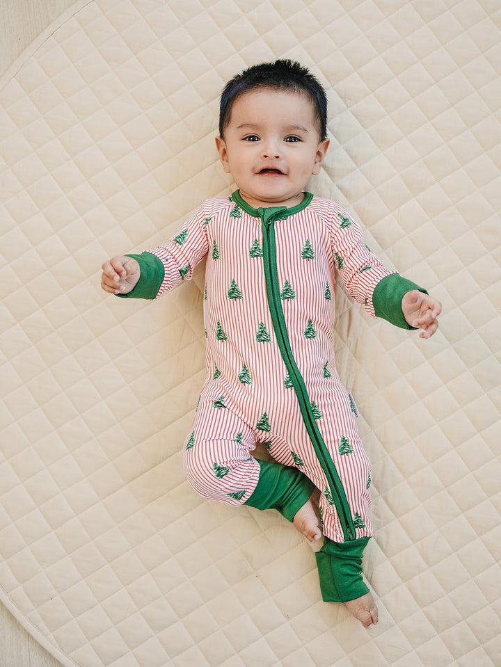 Baby lying on a quilt in the Magical Trees Christmas romper with one knee bent and feet uncovered.