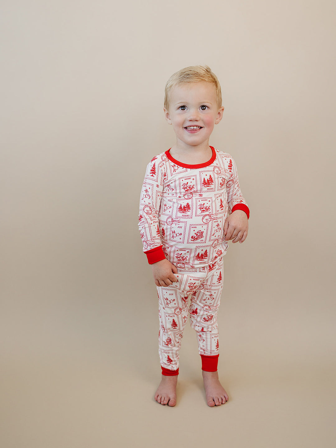 Front view of a smiling child wearing the North Pole Stamps Christmas pajama set with matching printed pants.