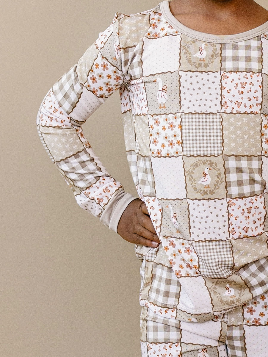 Close-up of a child wearing the Lucky Panda Kids Cottage Goose bamboo two-piece set in a neutral patchwork print.