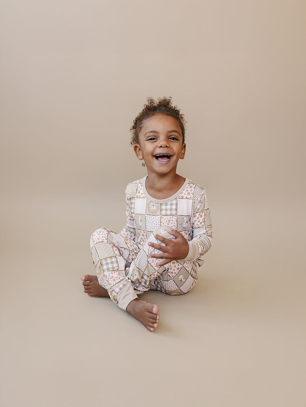 Smiling child sitting on a beige studio floor in the Cottage Goose bamboo two-piece set.