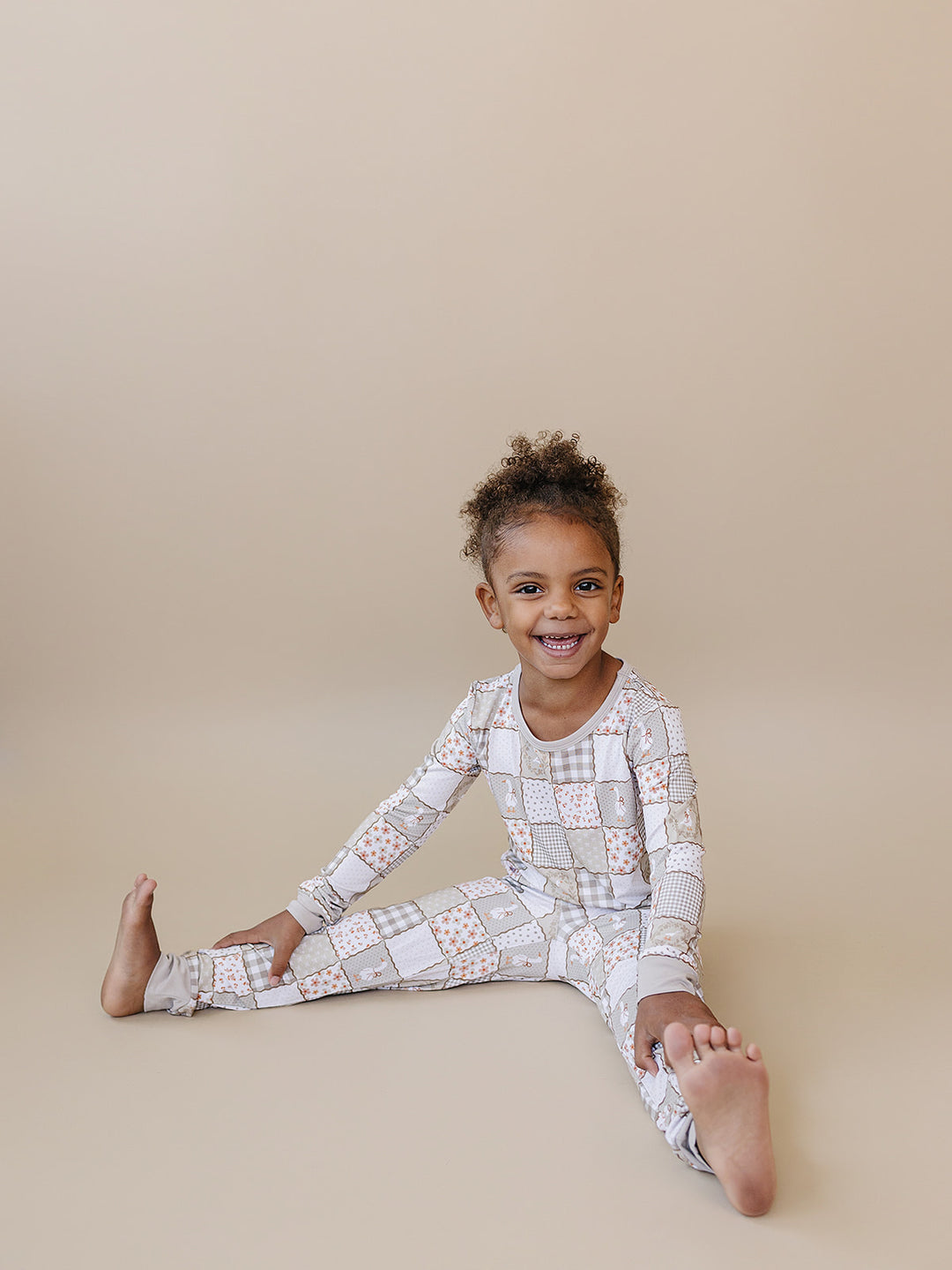 Smiling child sitting on the studio floor in the Cottage Goose bamboo set, showing its flexible fit for movement.