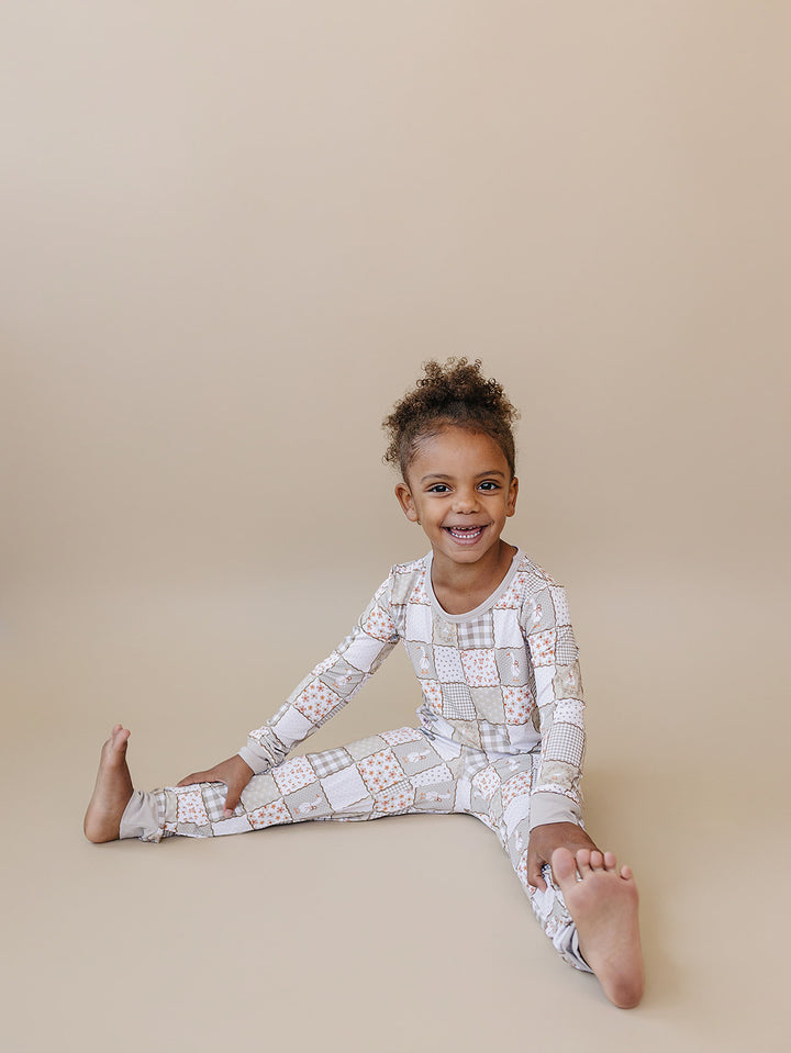 Smiling child sitting on the studio floor in the Cottage Goose bamboo set, showing its flexible fit for movement.