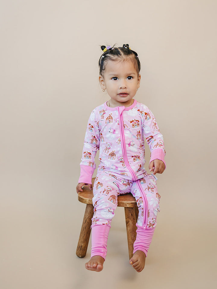 Toddler sitting on a wooden stool in the Pink Christmas zip romper with pink ankle cuffs.
