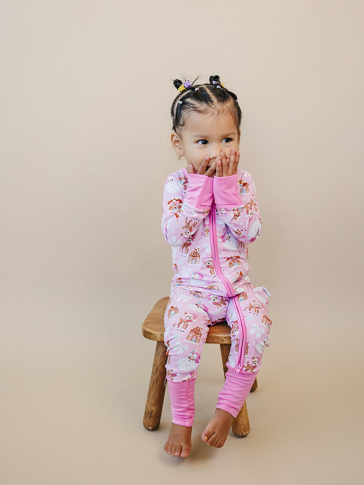 Toddler sitting on a stool with hands near their mouth while wearing the Pink Christmas zip romper.