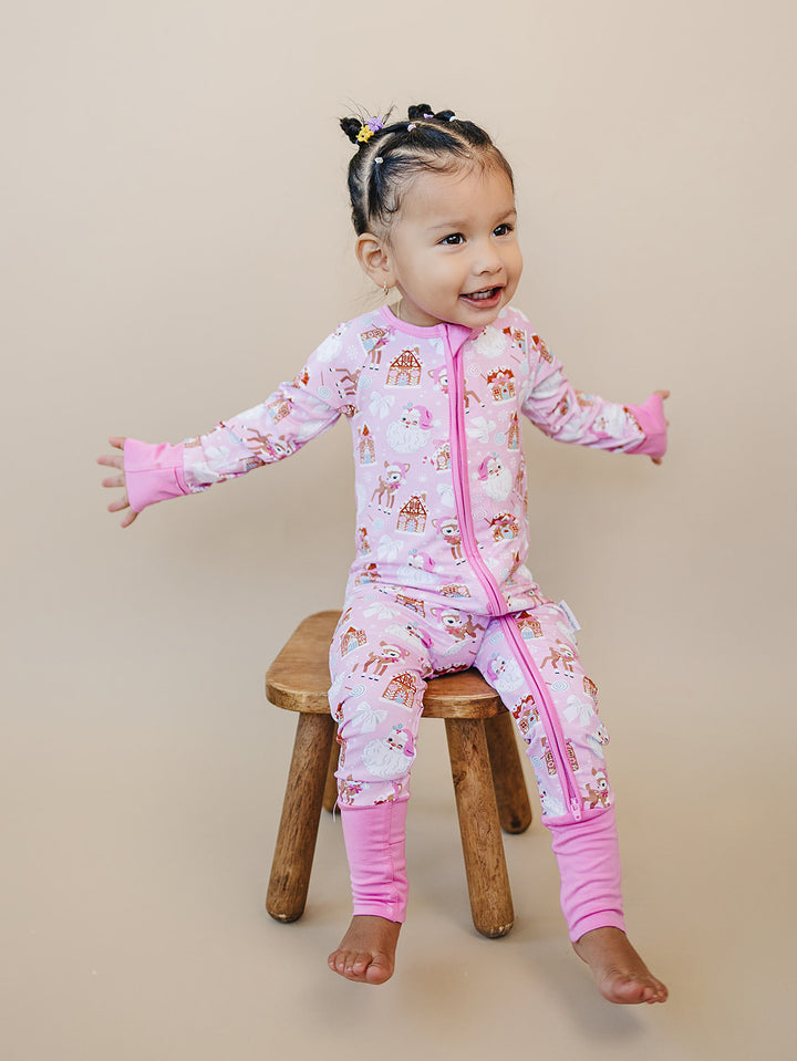 Smiling toddler sitting on a wooden stool with arms open in the Pink Christmas zip romper.