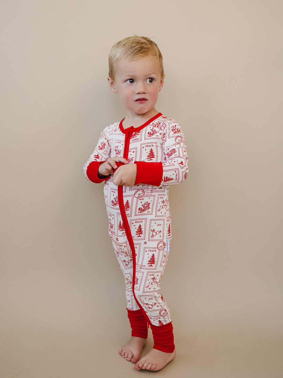 Toddler turned slightly sideways in the North Pole Stamps romper, showing the printed sleeve and red cuffs.
