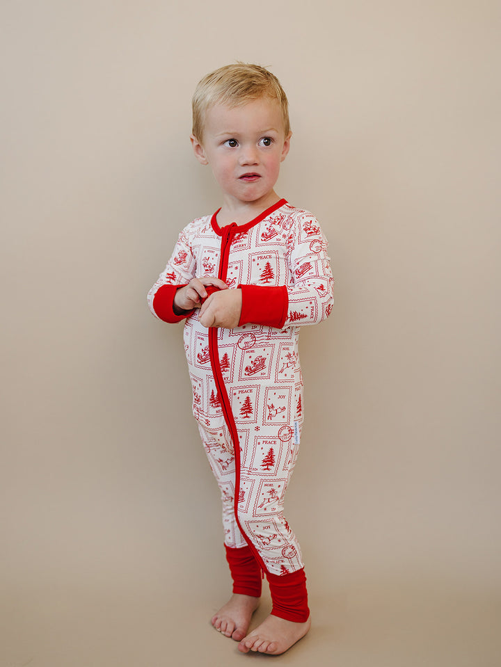 Toddler turned slightly sideways in the North Pole Stamps romper, showing the printed sleeve and red cuffs.