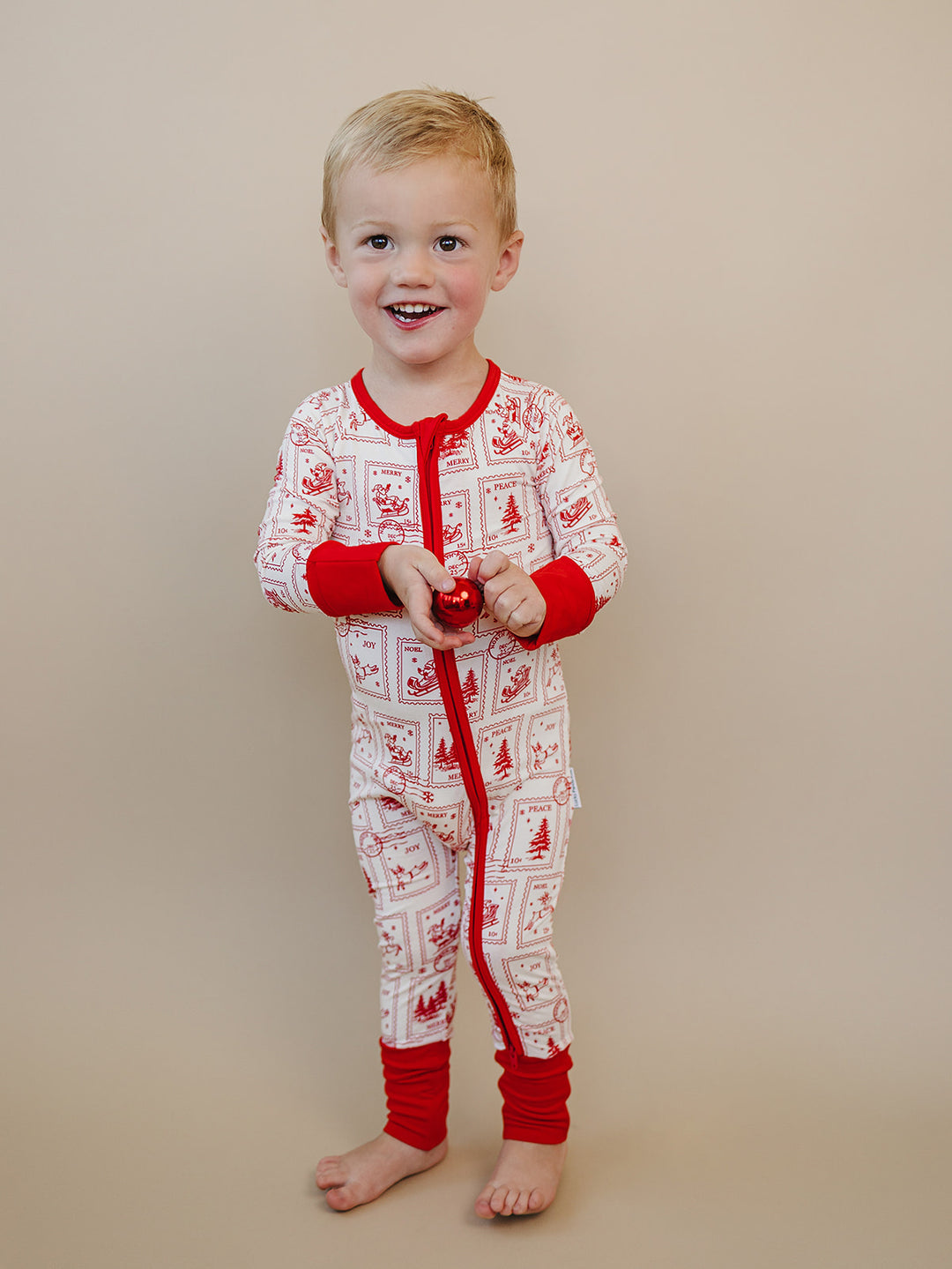 Smiling toddler wearing the North Pole Stamps Christmas zip romper, shown from the front.