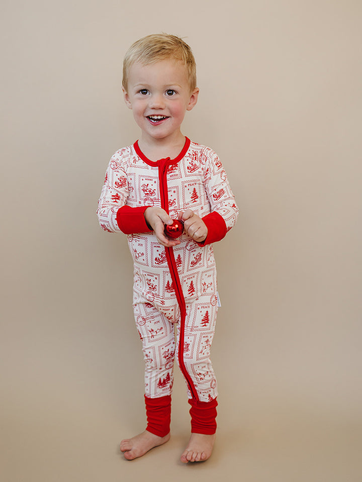 Smiling toddler wearing the North Pole Stamps Christmas zip romper, shown from the front.