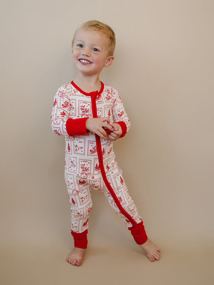Toddler standing in the North Pole Stamps Christmas romper with red wrist and ankle cuffs.