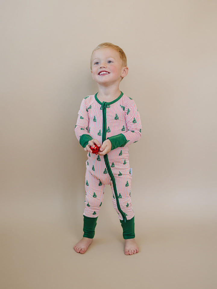 Toddler standing in the Magical Trees Christmas romper with green cuffs and a green front zipper.