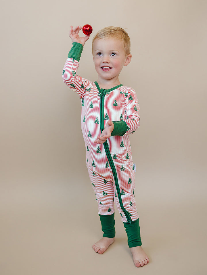 Toddler holding a red ornament overhead while wearing the Magical Trees Christmas romper with green trim.