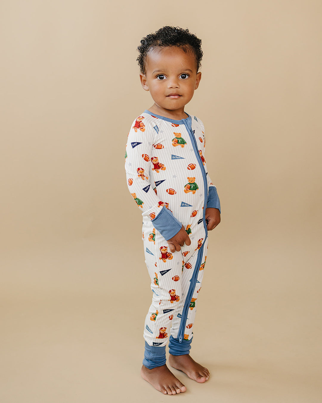 Child standing in the Touchdown Teddy bamboo romper against a neutral background.