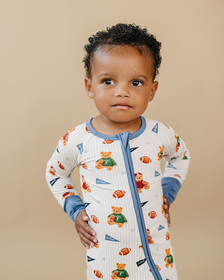 Toddler modeling the Touchdown Teddy bamboo zip romper against a neutral beige background.